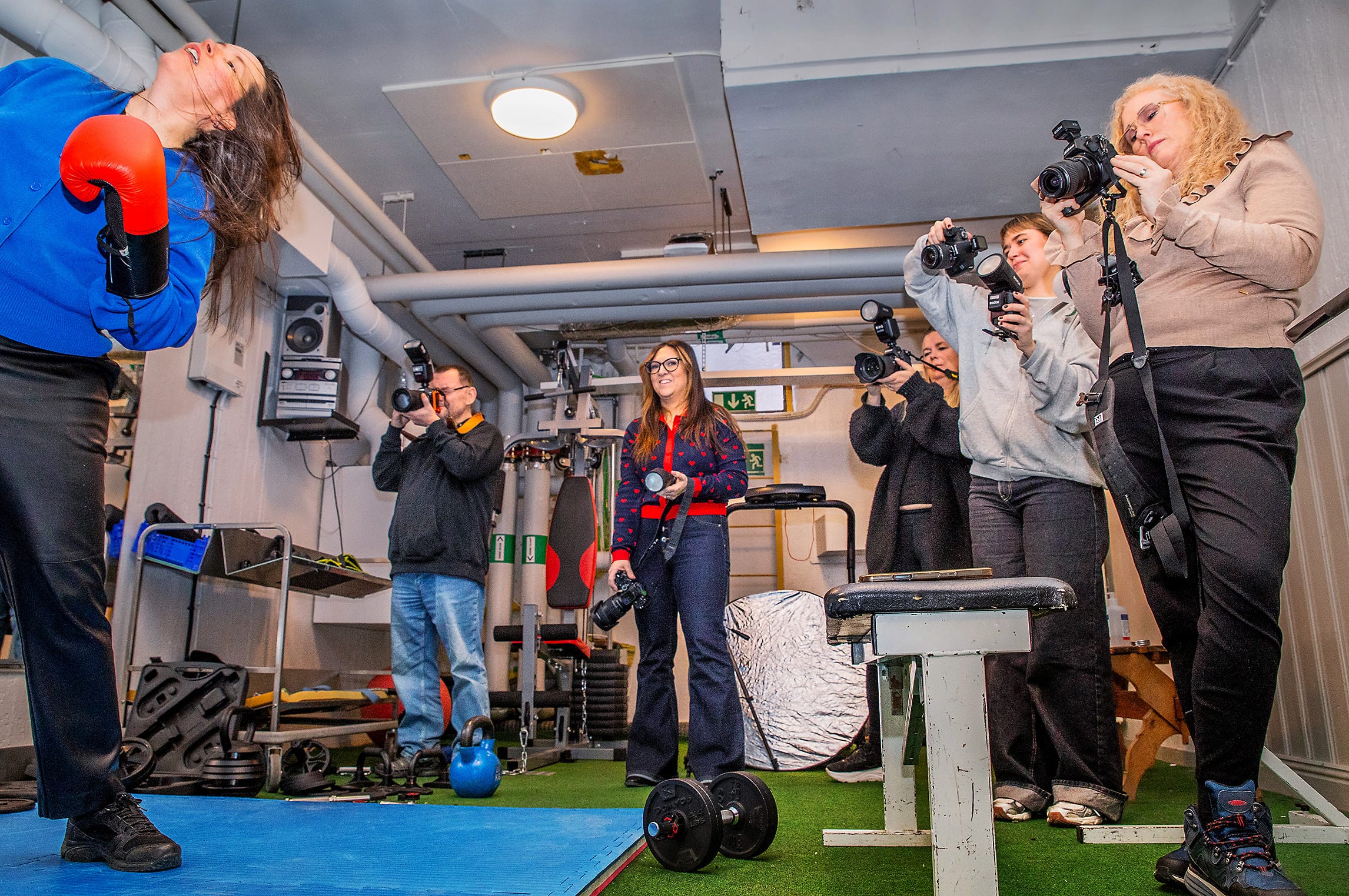 Flera personer fotograferar en kvinna som boxas i gym